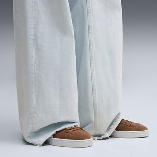 Brown suede sneakers with white rubber sole, worn with light blue jeans
