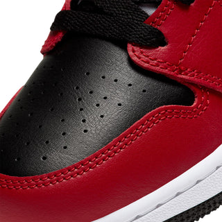 Close-up of youth sneaker toe and side panels in black with red overlays and perforations