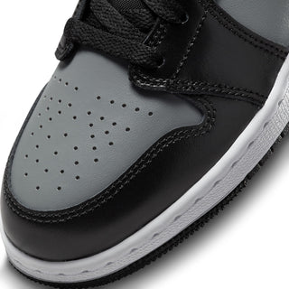 Youth mid-top sneaker close-up on toe: black leather, gray panel, lace detail, white sole