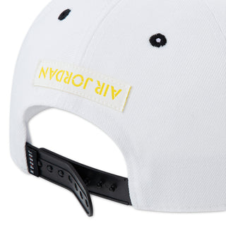 White snapback cap close-up with black strap and yellow logo label