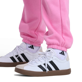 Pink fleece jogger pants with elastic cuffs and white logo, shown with sneakers