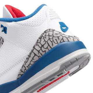 Kids sneaker close-up: white leather toe, cement grey pattern, blue sidewall, red accent.