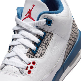 Youth white sneaker close-up with red Jumpman logo, blue lace loops, and elephant-print overlay