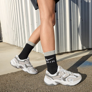 Model wearing white and gray sneakers with black socks showing AIR text and swoosh
