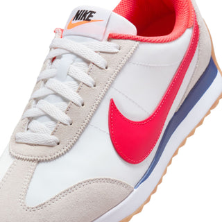 Women's sneaker upper close-up: white laces, red swoosh, beige panels, blue stripe