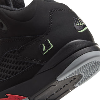 Black kids sneaker close-up with side stitching, green logo, and gray patterned outsole