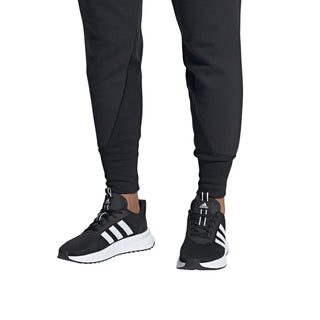 Men's black adidas sneakers worn by model, white stripes and white cushioned sole