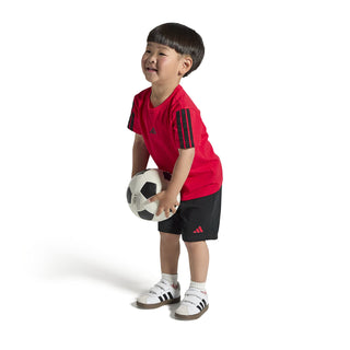 Toddler white sneakers on a child standing, with black 3-Stripes and gum sole.