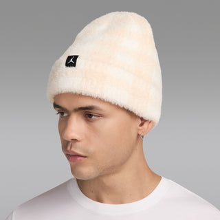 Cream plush beanie with black logo patch on front, side view