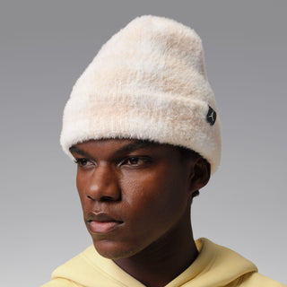 Cream plush beanie with black logo patch and ribbed cuff, side view