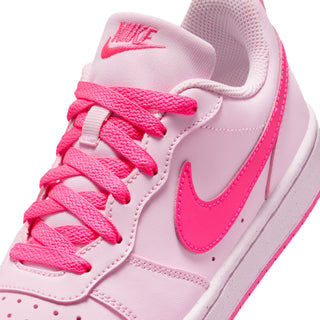 Youth pink low-top sneaker close-up with pink NIKE logo on tongue and lace-up detail