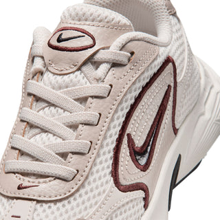 Close-up of kids light cream shoe upper with burgundy swoosh and lace eyelets