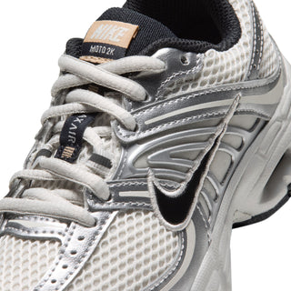 Close-up of Nike Air Max Moto 2K kids' sneaker, showing mesh, silver overlays, Swoosh and laces.