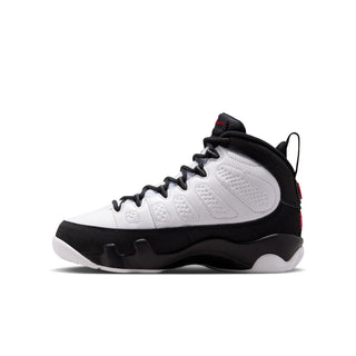 Side view of youth mid-top sneakers in white and black with red lace tag