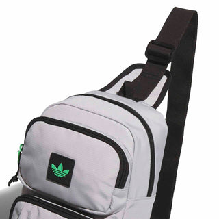 Light grey crossbody sling bag with adjustable black strap and front patch logo