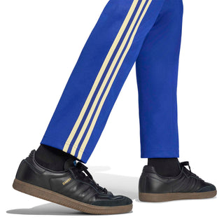 Men's blue track pants with gold triple stripe on leg and tapered ankle cuffs