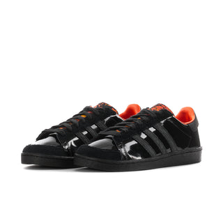 Pair of black low-top sneakers with glossy finish, orange laces, and stripe details