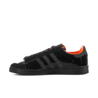 Black low-top sneakers with orange-lined collar, textured strap, and three stripe panels