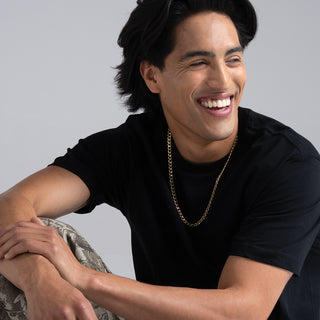 Man wearing a black t-shirt and gold chain, sitting against a gray background