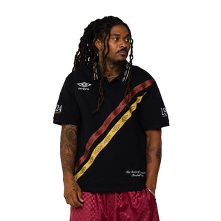 Black men’s polo shirt with Umbro logo, diagonal red-yellow stripe, and small chest text