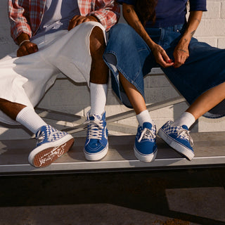 Men's low-top Vans sneakers worn with denim jeans, blue checker accents and white soles