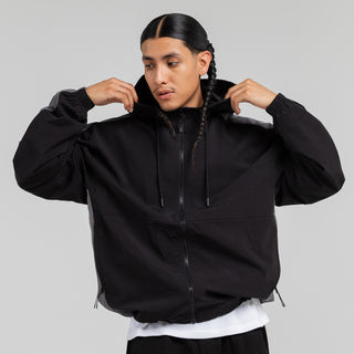 Men's black windbreaker jacket with adjustable hood and full-zip; model holding cuffs.