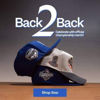Two baseball caps with championship logos on a wooden surface, promotional text 'Back2Back' and 'Shop Now' button.