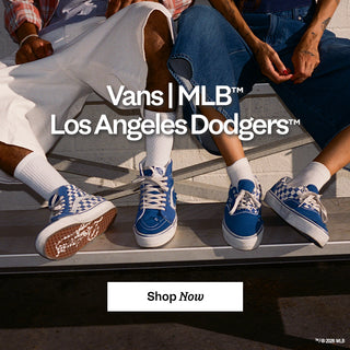 Two people seated on bleachers wearing blue-and-white Vans x MLB Los Angeles Dodgers sneakers with checkerboard details. Shop now.